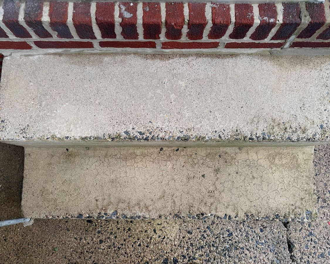 The same Lansdowne, PA front steps from above after washing, the treads clean pale concrete and the brick wall above them bright