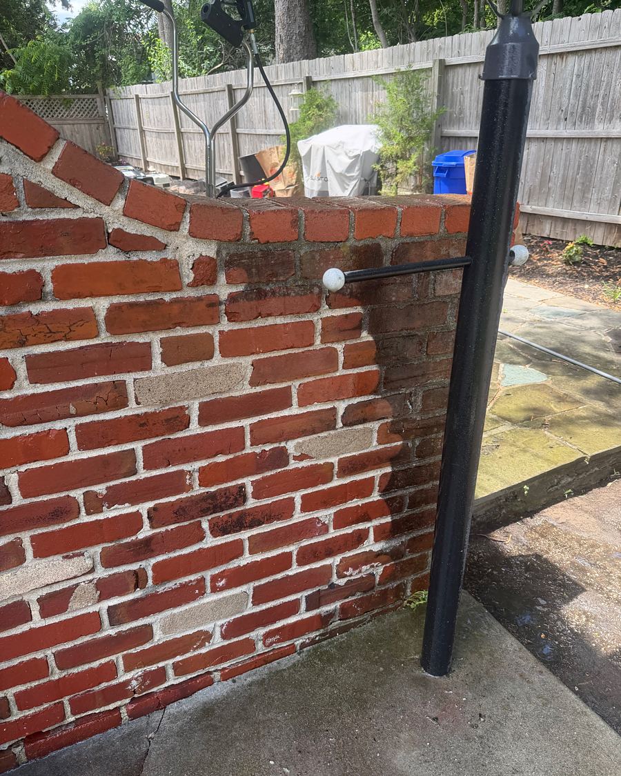 Red brick garden wall in Havertown, PA partway through washing, clean brick beside brick still dark with grime