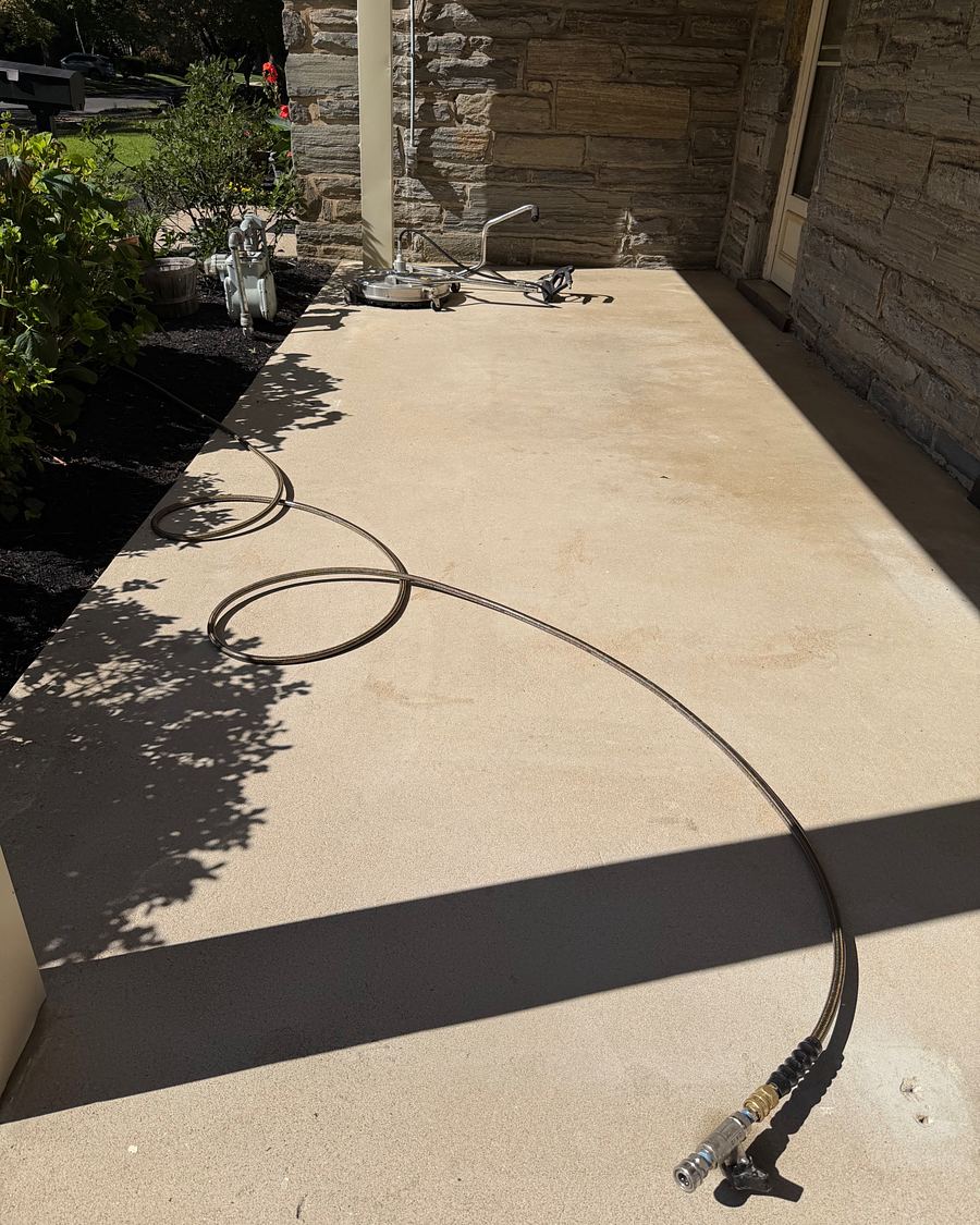 A clean concrete porch in Drexel Hill, PA with the surface cleaner and pressure hose still lying on it