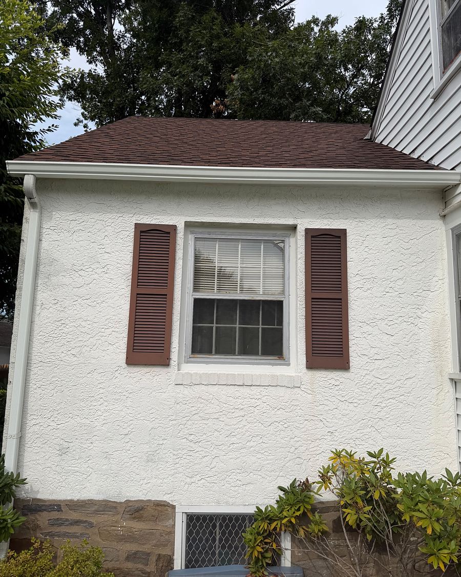 White stucco side elevation of a Havertown, PA cape with brown shutters, gutters clean after brightening