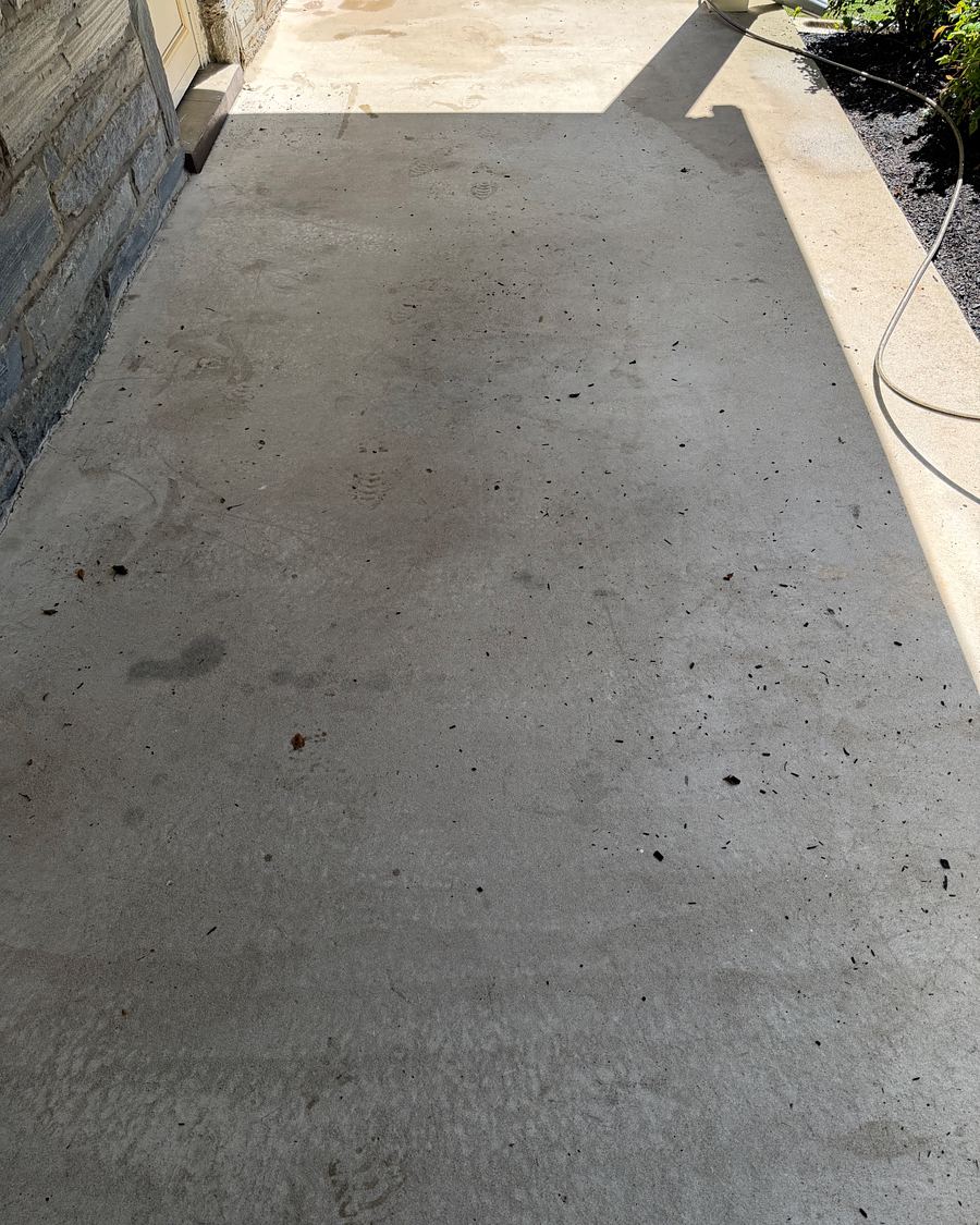 Concrete floor of a covered stone porch in Drexel Hill, PA before washing, gray with dark spots and footprints