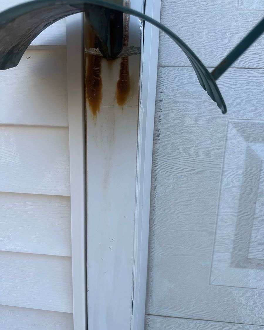 Orange rust streaks running down a white vinyl corner post under a hose hanger in Hatboro, PA