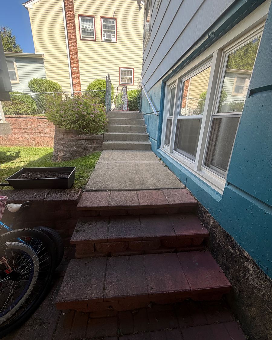 Side walkway and brick steps beside a blue house in Havertown, PA before washing, the concrete dark