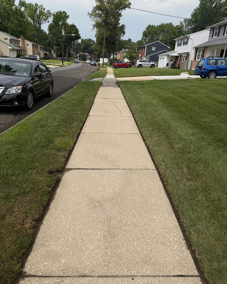 The same public sidewalk after pressure washing, clean pale concrete running the length of the block