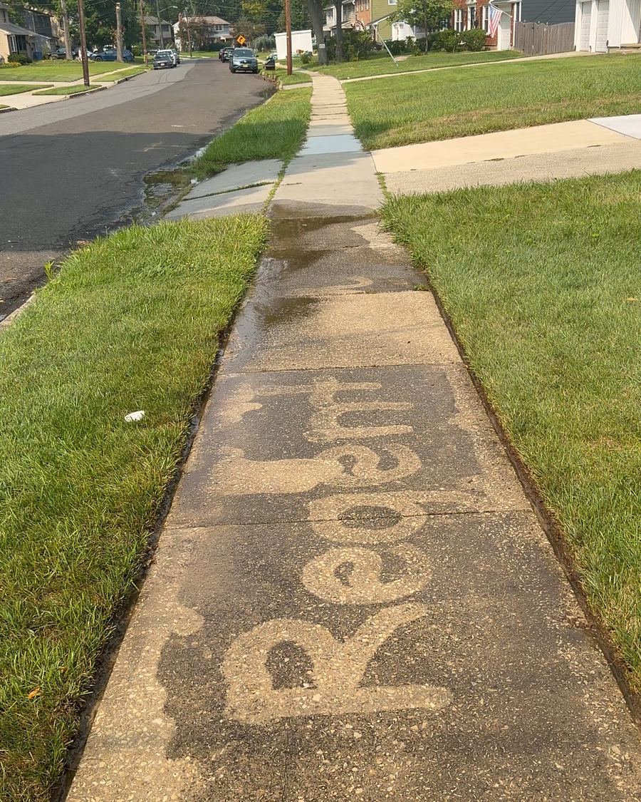 A concrete sidewalk with the word Regent cleaned into the surface, the rest of the path still dark with grime
