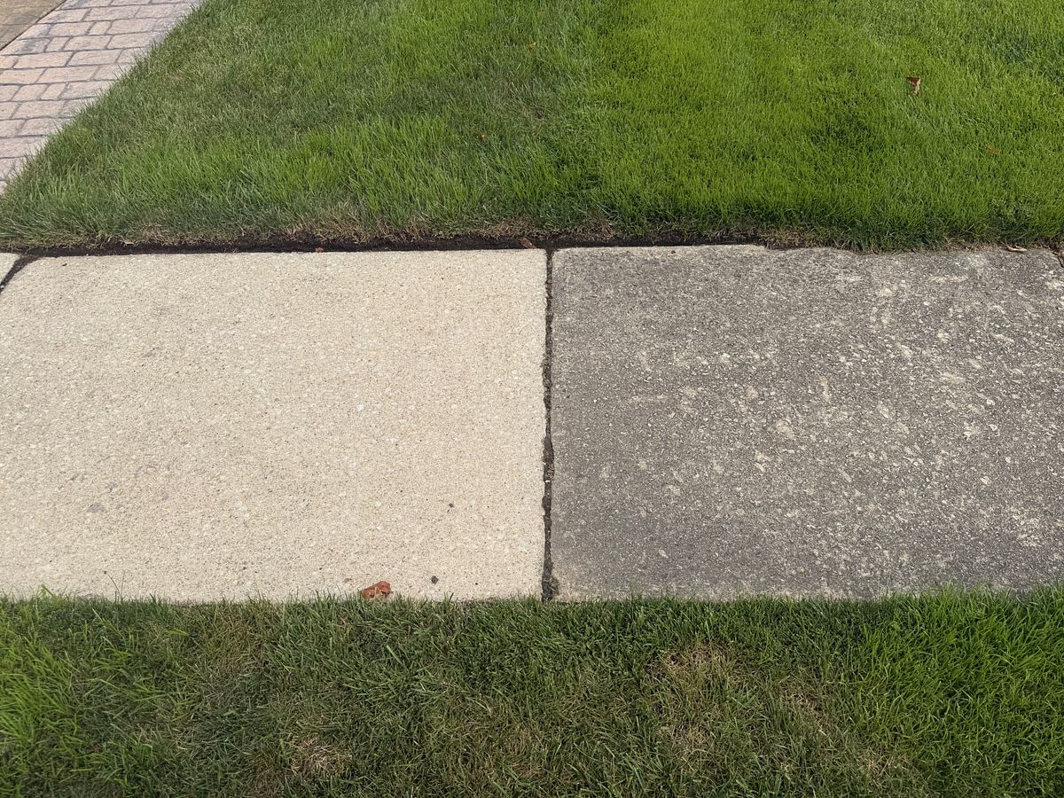 Two concrete sidewalk slabs side by side, the left one pressure washed to a pale cream and the right one still dark gray with grime