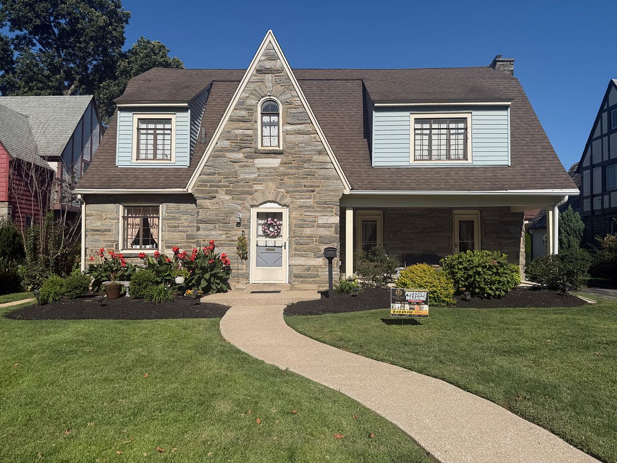Stone Tudor-style home with light blue siding dormers in Drexel Hill, PA after washing, a clean curved walkway crossing the lawn to the front door