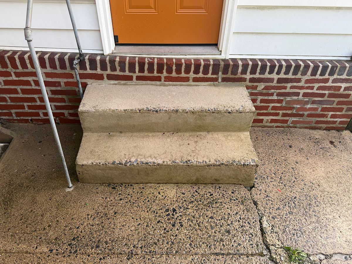 Clean concrete front steps and walkway of a brick twin in Lansdowne, PA after pressure washing, the orange front door above them